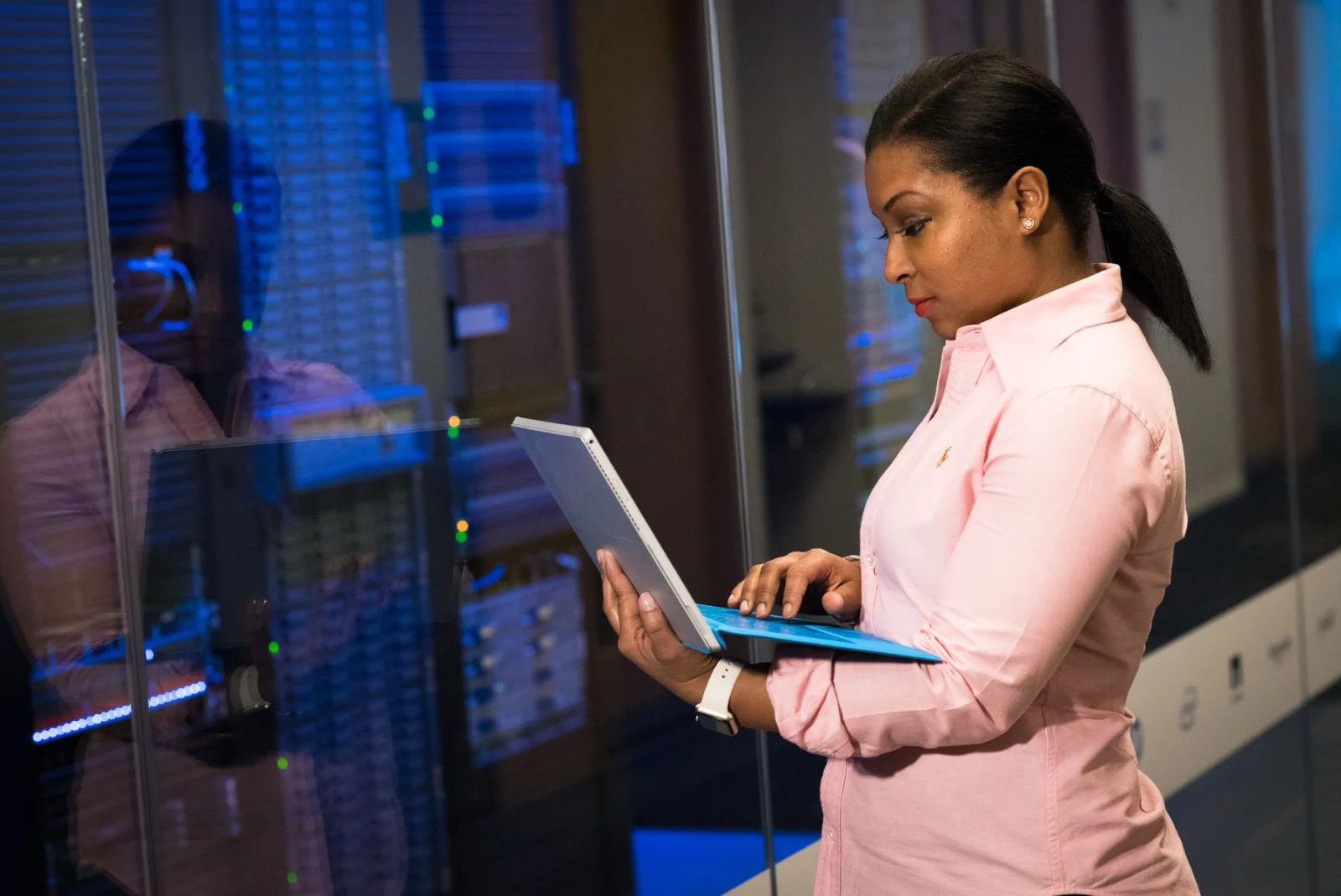 An IT infrastructure engineer reviewing device status on a laptop beside a server room